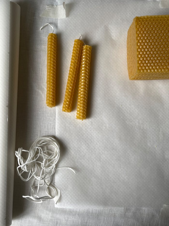 A top-down view of beeswax sheets, wax candles, and string on a white background.